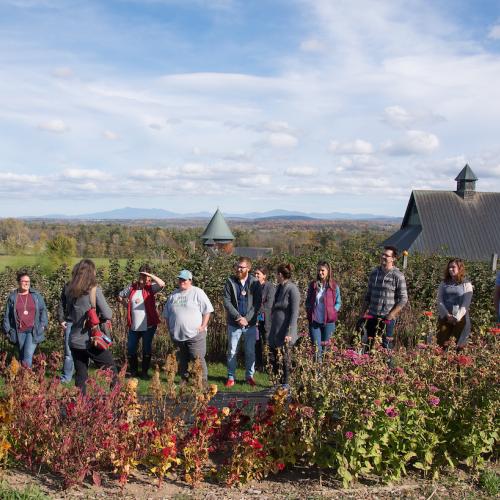 A line of educators stand in a garden behind a large barn