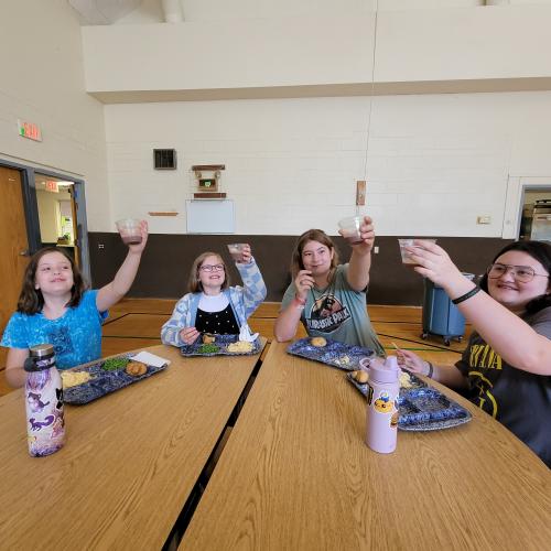 Kids raise up cups of milk in a "cheers" motion around a lunch table