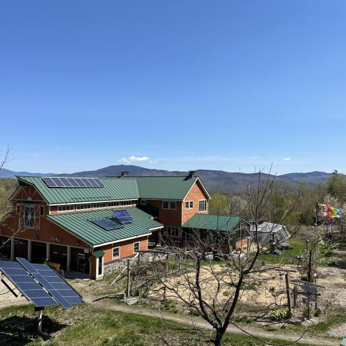 community building of the hummingbird center; framed by solar panels, flowering serviceberries, mountain ridges, and our kitchen garden
