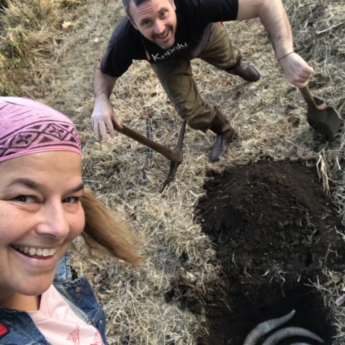 Two people stand next to a dug pit of soil