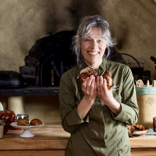 Heike Meyer of Brot Bakehouse stands before her baking table and earthen oven holding sourdough bread