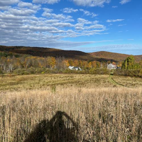 A view of a Vermont farm field looking down a hill toward a farmhouse and barn