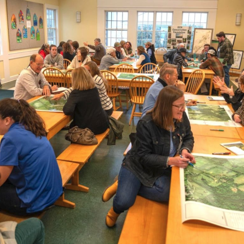 Room of people sitting at tables with maps