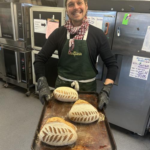 Baker holding tray of sourdough loaves