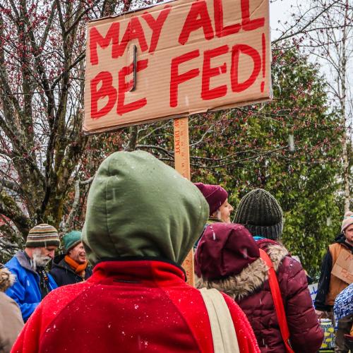 A crowd of farmers, farmworkers, and NOFA-VT members at the Middlebury Farmer Day of Action, with a sign reading "May All Be Fed"