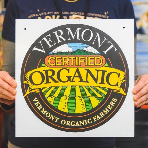 A farmers hands holding a Vermont Certified Organic seal
