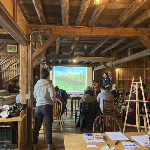 People attending a presentation in a rustic wooden room with a nature image projected on a screen.