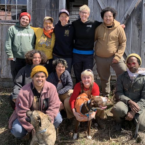 A group photo of the farmers that make up Rock Steady Farm posting with smiles and a few farm dogs in front of their barn