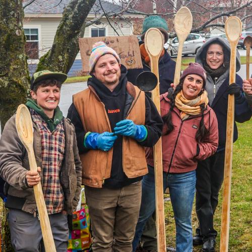 NOFA-VT farmer-members Stoni Tomson, Jacob Powsner, and Jess Purks stand with ACORN-VT Executive Director Lindsey Berk holding giant hand-carved wooden spoons inspired by the Parable of the Long-Handled Spoons