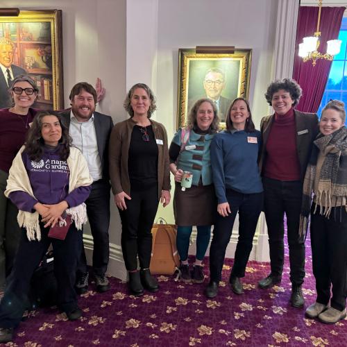 NOFA-VT Grassroots Organizer Jess Hays Lucas, NOFA-VT farmer-member Melisa Oliva, Farm to Plate Director Jake Claro, Vermont Food Security Roadmap Coalition Manager Becka Warren, Action Circles Political Stragetist Amy Shollenberger, NOFA-VT Policy & Organizing Director Maddie Kempner, Rural Vermont Legislative Director Caroline Gordon, and Vermont Farm Fund Manager Kristin Blodgett stand arm in arm smiling at the Vermont State House after a successful day of lobbying in support of S.60
