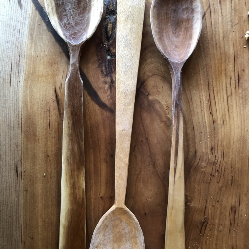 three hand-carved wooden spoons lie side-by-side on a wooden counter top.