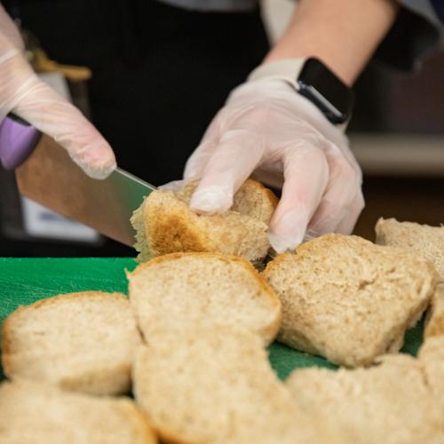 A Vermont school nutrition specialist slices local rolls made with local grains on a green cutting board.