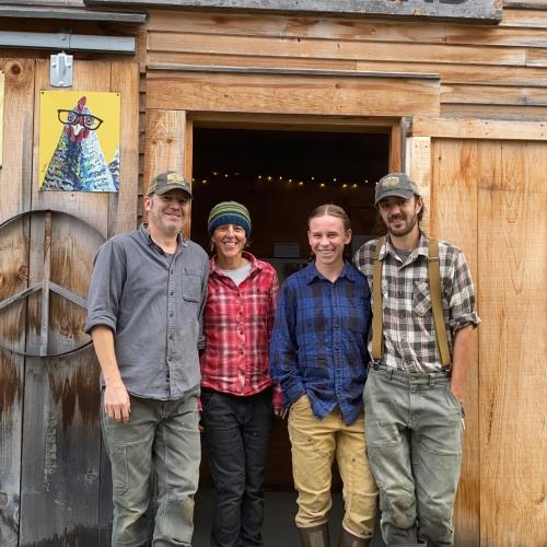 The farmers from Firefly Farm standing arm-in-arm and smiling in front of their barn