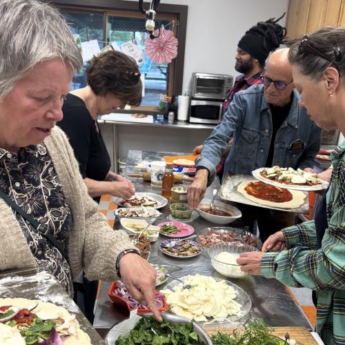 Five people top homemade pizzas around a kitchen island.