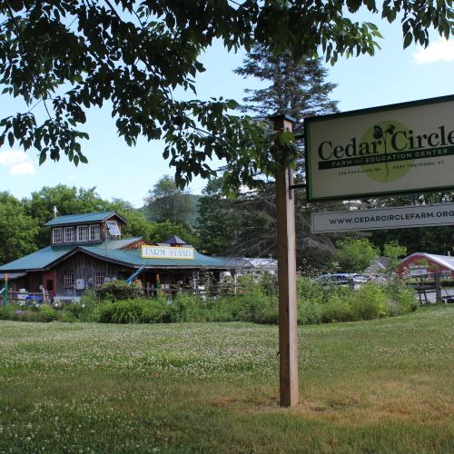 The roadside sign for Cedar Circle Farm in the foreground with the farm stand and several other outbuildings in the background