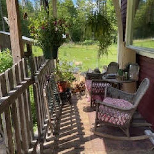 Picture of a wooden porch with wicker chairs, hanging plants, and wind chimes.