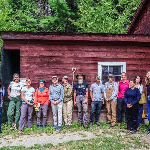 Vermont farmers lined up along the side of a red barn at Honey Field Farm with Senator Peter Welch and his staff, along with staff from NOFA-VT's policy & organizing team 