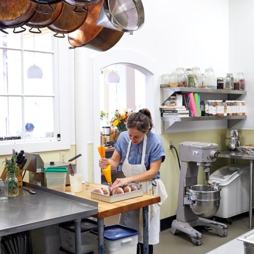 Copper jam pans hanging over work tables at Minifactory as a baker fills donuts 